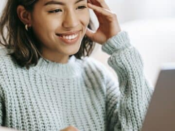 Hispanic woman working remotely on laptop near notepad in apartment