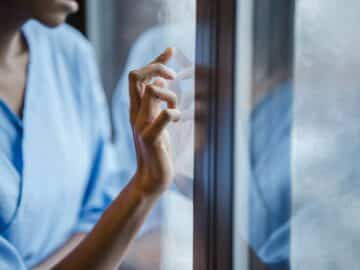 Black woman touching window while healing in hospital