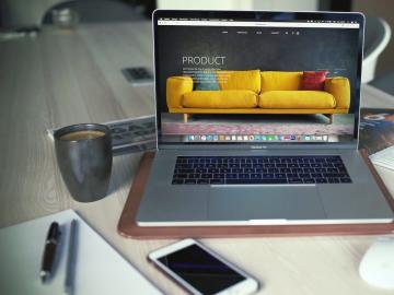 A laptop next to a silver coffee mug on top of a light wooden desk