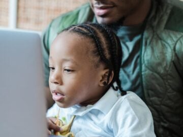 A father and child bonding while using a laptop indoors, showcasing family and technology.