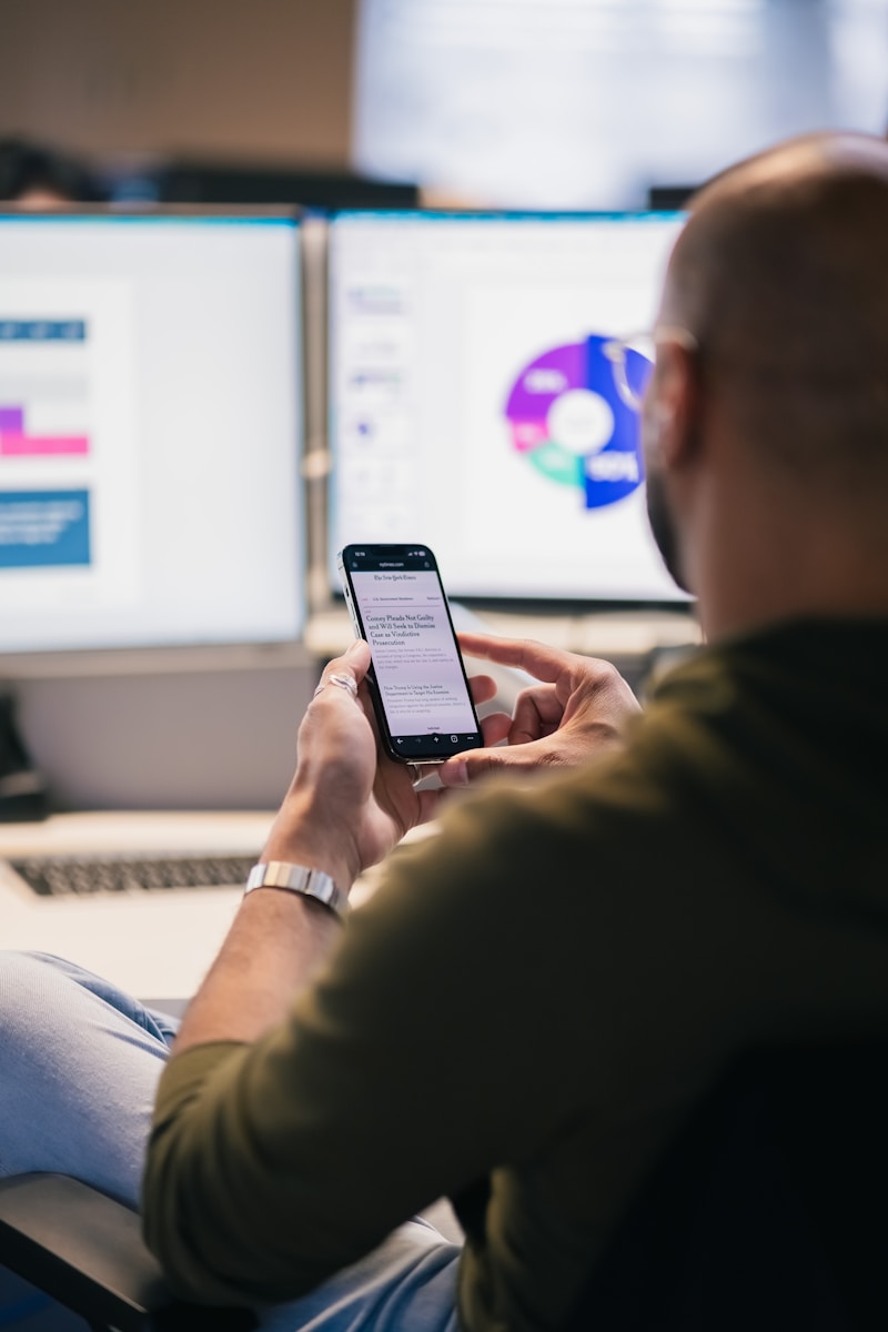 Man using smartphone in front of computer monitors.