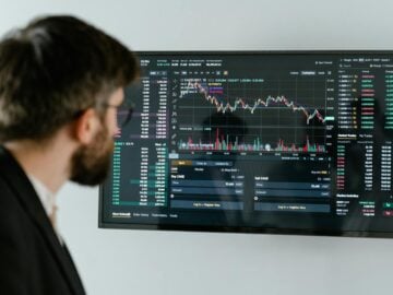 A businessman in a suit looks at a screen displaying stock market charts and data analysis.