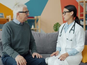 Doctor talks with an elderly patient on a couch.