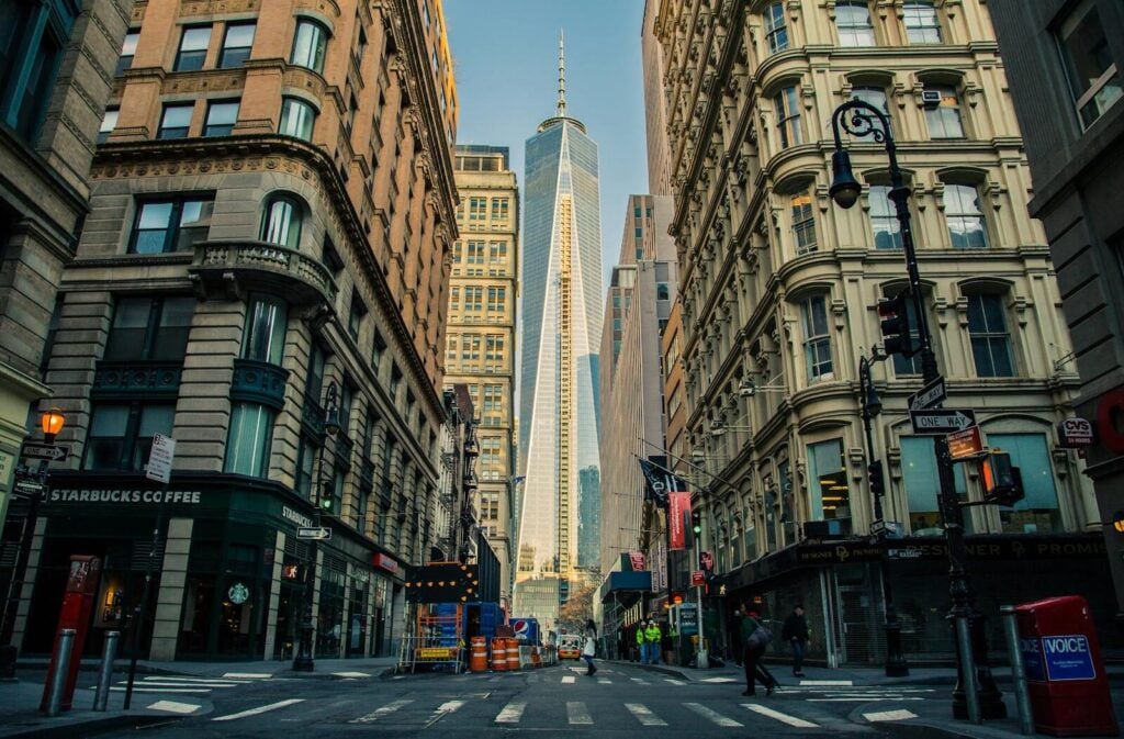 Street view of One World Trade Center in New York City surrounded by urban architecture and city life. budget travel tips expensive cities usa