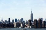 A stunning view of the New York City skyline featuring the iconic Empire State Building under a clear blue sky. budget travel tips expensive cities usa
