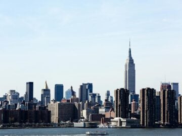 A stunning view of the New York City skyline featuring the iconic Empire State Building under a clear blue sky. budget travel tips expensive cities usa