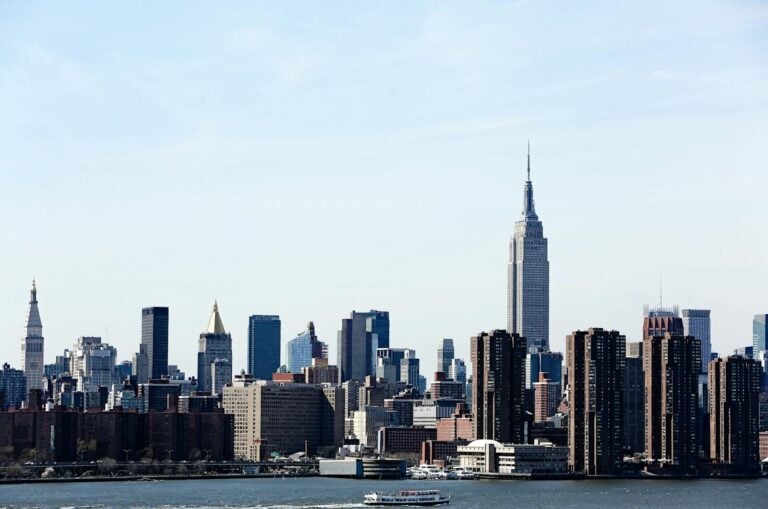 A stunning view of the New York City skyline featuring the iconic Empire State Building under a clear blue sky. budget travel tips expensive cities usa