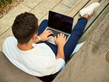 man wearing white sweatshirt using laptop computer sitting on sofa chair