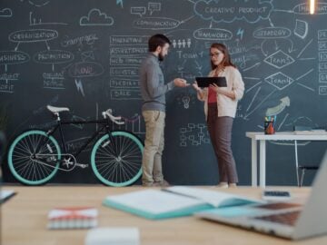 Two people discuss a plan on a chalkboard wall.
