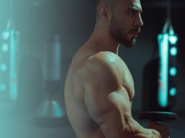 a shirtless man holding a barbell in a gym