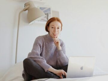 woman in gray sweater sitting on chair using macbook