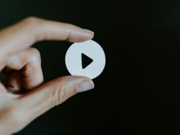 a hand holding a white paper cut out of a video play button